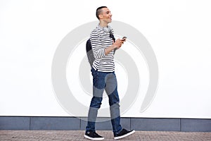 Side portrait of happy young man walking with bag and mobile phone against white wall