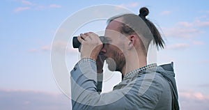 Side portrait of hipster bearded man looking into binoculars afar handheld camera slow motion. Authentic man with