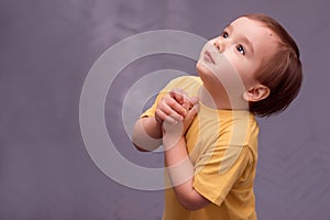 Side portrait of a little boy begging or asking for something against grey painted floor