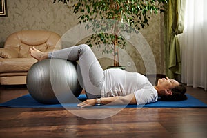 Side portrait of a pregnant woman doing prenatal healthy relaxation exercises with a fitness ball on a yoga mat at home