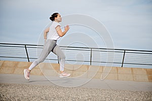 Side portrait of a woman running on the city bridge, performing her morning jog, exercising outdoors