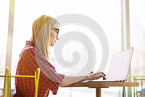 Side portrait young woman worker sitting in office while using laptop computer and typing by keyboard