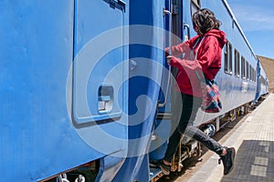 Side profile of a female tourist embarking a blue train carriage. Vertical image