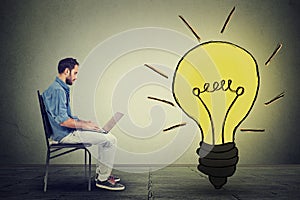 Side profile man using laptop with light bulb on gray wall background