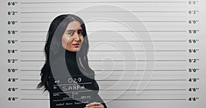 Side profile mugshot of beautiful woman turning head and looking to camera. Female mixed race criminal holding sign for