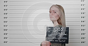 Side profile mugshot of female person holding sign while being photographed in front of metric lineup police station