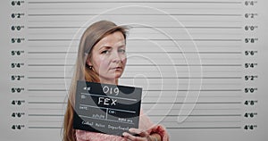 Side profile mugshot of female person with long hair turning head and looking to camera. Criminal woman holding sign for