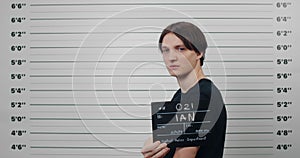 Side profile mugshot of male person with dark hair turning head and looking to camera. Criminal young man holding sign