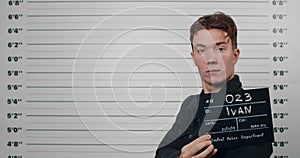 Side profile mugshot of male person with red hair turning head and looking to camera. Criminal young man holding sign