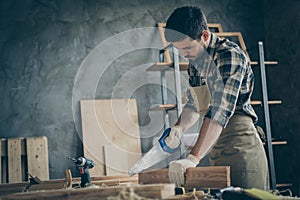 Side profile photo of serious confident focused man cutting off unneeded pieces of wooden block using saw