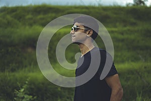 A side profile portrait of a young indian boy wearing black sunglasses with green fields in the background