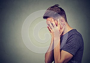 Side profile of a sad young man with hands on face looking down. Depression and anxiety disorder photo