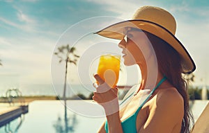 Woman wear straw hat drinks orange juice relaxing near pool