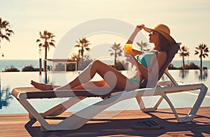 Woman in bikini drinks cocktail sunbathing on deckchair near pool