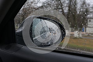 Side rear view mirror through the glass in rainy weather. Reflection of car headlamps.