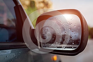 Side rear-view mirror on a modern car. Rainy water drops on glass