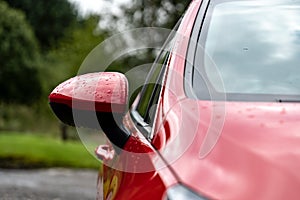 The side rear-view mirror of the red modern aerodynamic car with small depth of field andwater drops