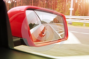 Side rearview mirror of a red car, roadside and highway reflection