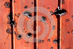 Side of shipping container rusted metal plate heavily damaged by shrapnel during war covered with faded dilapidated paint