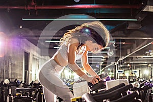 Side shot of attractive young brunette sportswoman riding exercise bike during cycling workout in gym.