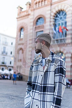 Side shot of a Caucasian young man with a plaid jacket looking left in the street, vertical shot