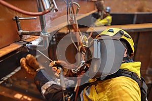 Side shot close up of industrial rope access welder maintenance abseiler wearing fall safety body harness helmet PPE photo