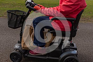 A side on shot of an elderly lady in a red coat enjoying the freedom of an electric mobility scooter