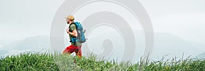 Side shot of hiker man walking by the foggy cloudy weather mountain range path with backpack. Active sport backpacking healthy