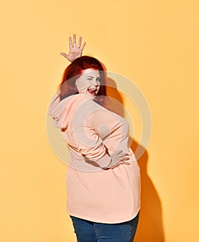 Side shot of joking positive chubby young female standing with hands on hips, giving a wink and lolling.