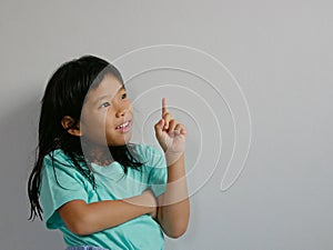 A side-shot portrait of surprised, excited, little girl, 5 years old, pointing her finger up on a white blank background, copy