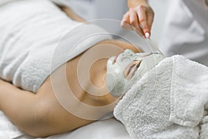 Side shot of a woman laying down in a towel and having put a clay face mask. Beauty concept. Spa concept.
