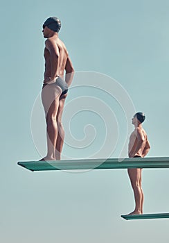Side by side on the dive. Full length shot of two handsome young male athletes standing on diving boards outside.