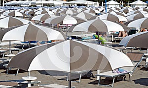 Side and top view of beach umbrellas with sun beds and unrecognizable people.