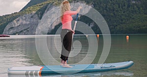 Side tracking of woman paddling on sup board at Wolfgangsee mountain lake, Austria, early morning. Active tourism and travel.