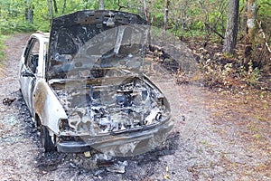 Side view of abandoned burned out car left on side of the road with hood left open expose burned engines