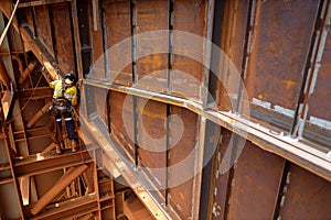 Side view of abseiler rope access repairer hanging in fall restraint position performing oxy acetylene cutting metal beam photo