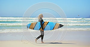 Side view of active senior Caucasian female surfer walking on beach in the sunshine 4k