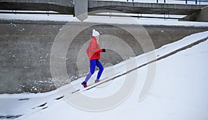 Side view of active senior woman running up the stairs outdoors in snowy winter.