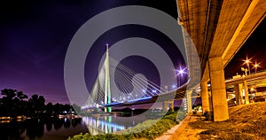 Side view of Ada bridge at night with reflection over Belgrade marina on Sava river