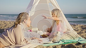 Side view of Adorable daughter talking with parent in romantic tent on beach 4K