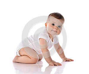 Side view of adorable infant baby in diaper and white bodysuit is crawling on all fours looking at camera