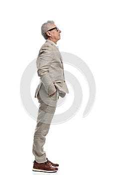 side view of adult in his 60s holding hands in pockets and standing in line