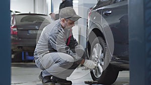 Side view of adult professional tightening screws on car wheel. Caucasian male auto mechanic working in auto repair shop