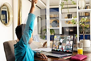 Side view of african american boy raising hand while attending online class over laptop at home