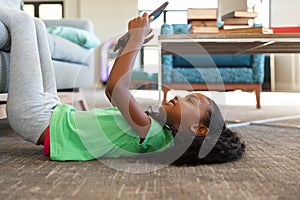 Side view of african american elementary girl using digital tablet while lying on carpet in school