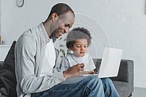 side view of african american father watching something at laptop with son