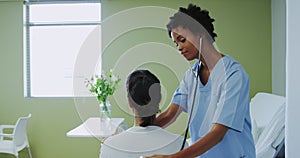 Side view of African american female doctor examining female patient in the ward at hospital