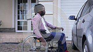 Side view African American man rolling wheelchair to car opening driver's seat door. Portrait of motivated confident