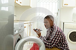Man talking on mobile phone while putting clothes in washing machine in kitchen