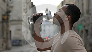 Side view african american runner drinking water from the sport bottle after the scamper. Man feels thirsty after